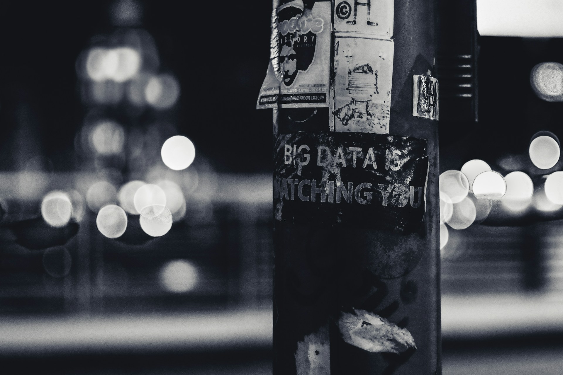 A black and white photo of a telegraph pole with a torn sticker saying BIG TECH IS WATCHING YOU
