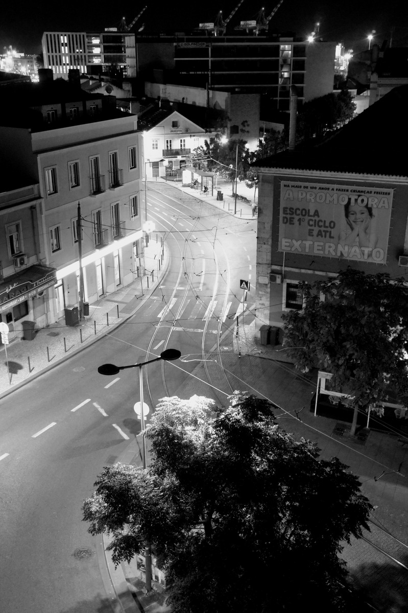 Black and white photograph showing buildings and tram tracks, illuminated by street lights