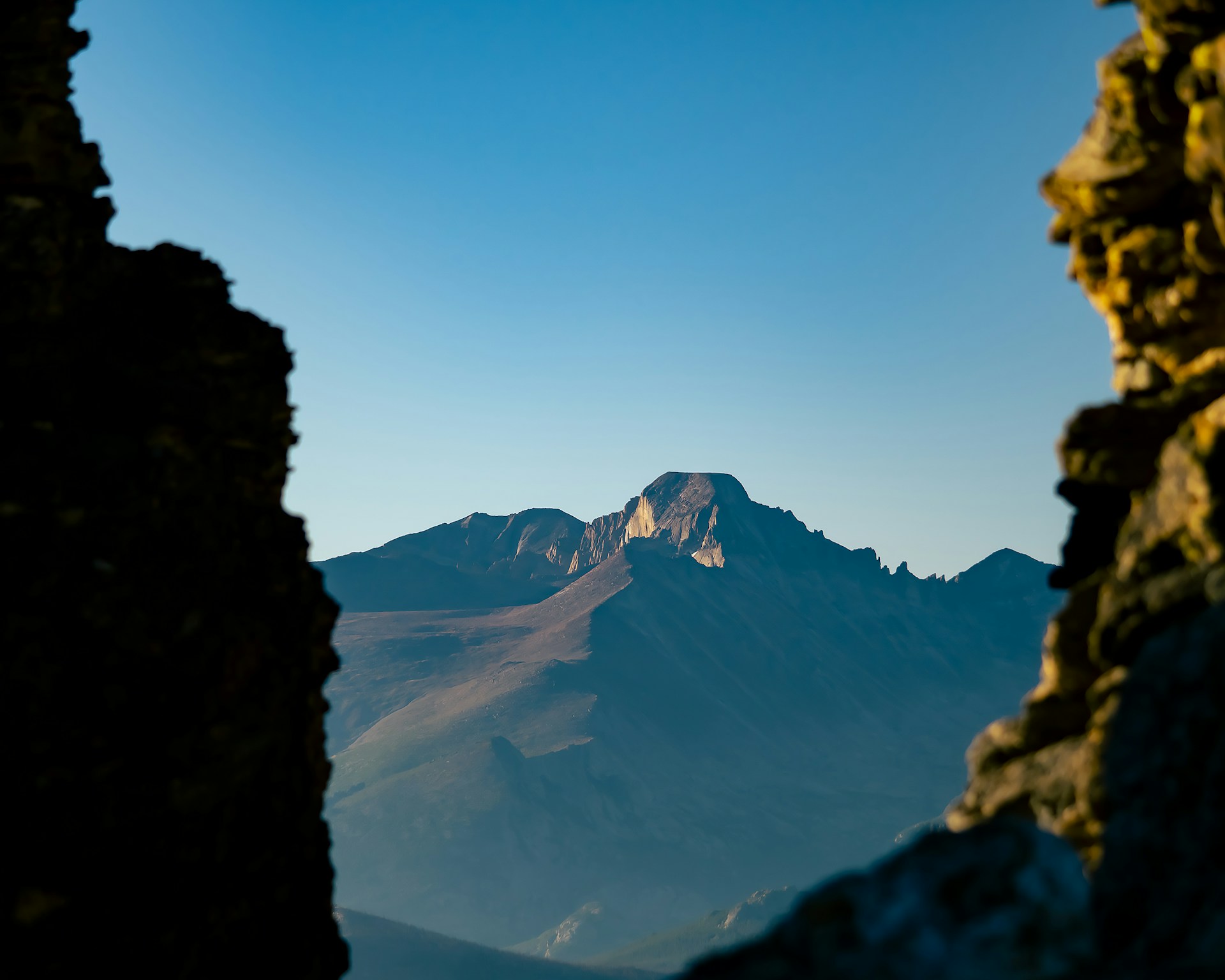 Peering through a canyon at distant mountains. An epic landscape that inspires thought. The cool lighting is relaxing as the sun reflects off the mountains causing a blue hue that evokes wisdom.